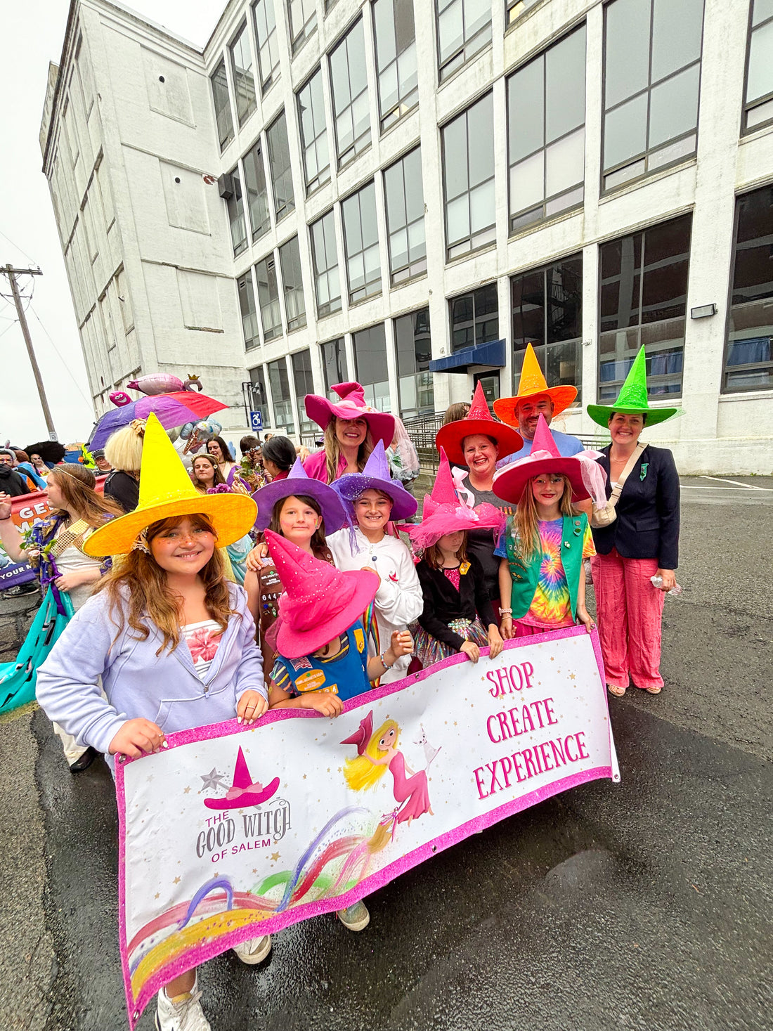 Group of people with colorful rainbow hats holding a banner about the good witch of salem. They are about to start marching for the parade