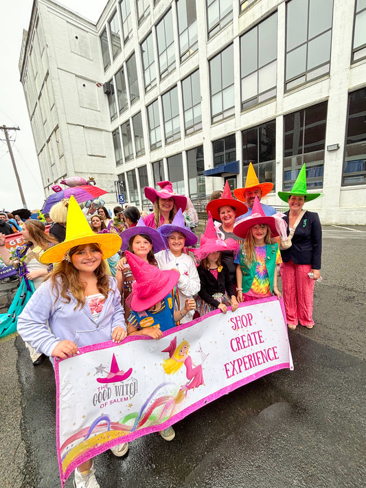 Group of people with colorful rainbow hats holding a banner about the good witch of salem. They are about to start marching for the parade